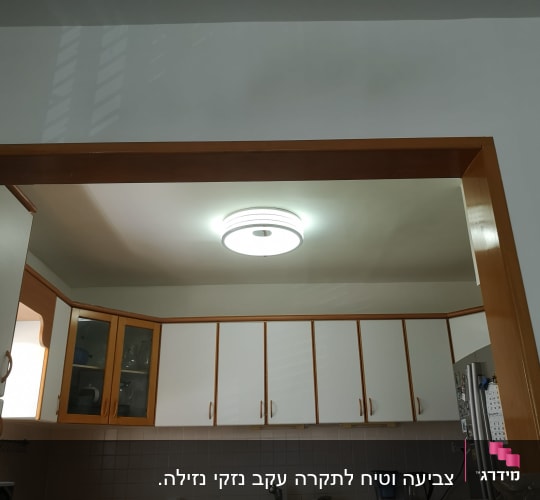 מטבח עם ארונות לבנים ותאורה עגולה בתקרה